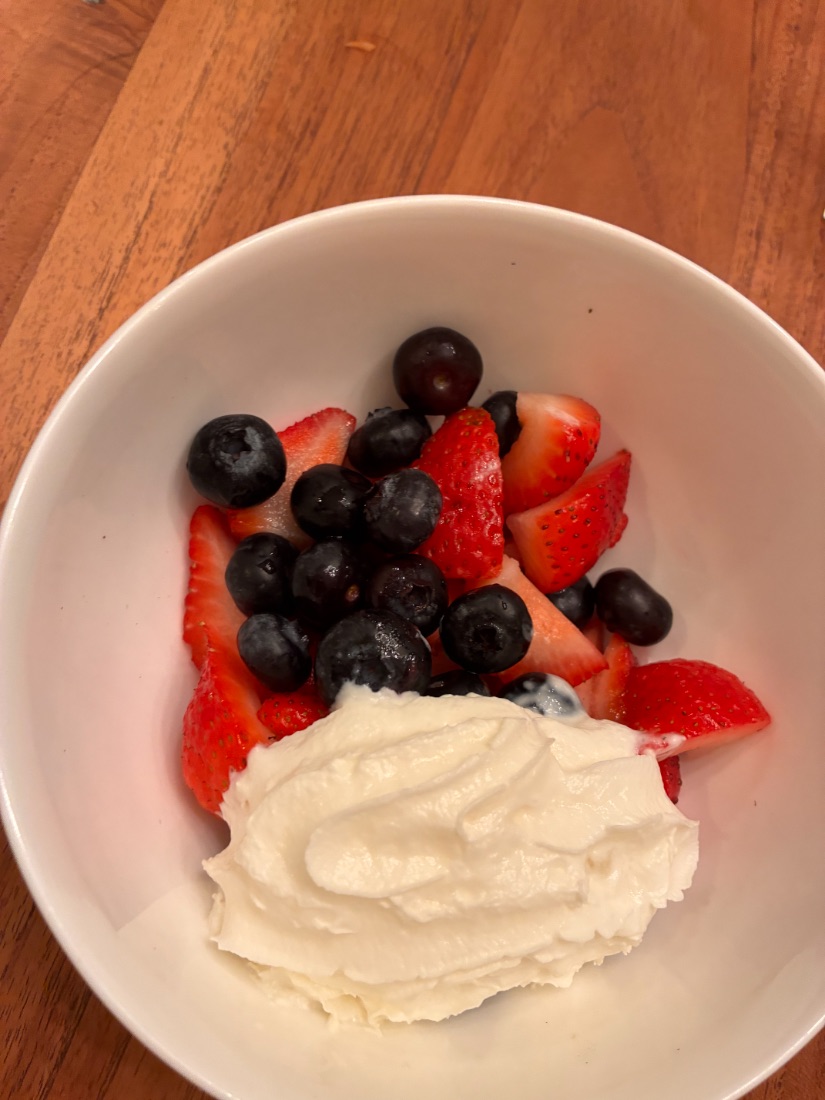 A bowl of strawberries and blueberries with whipped cream